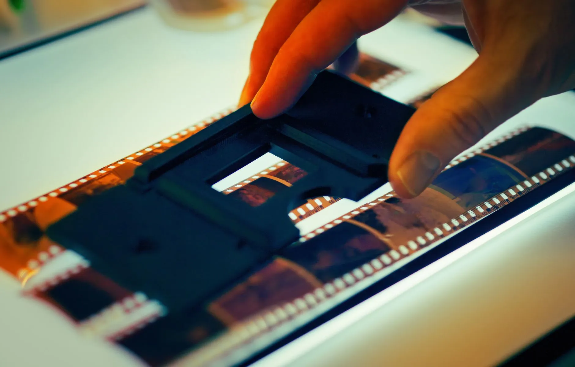 A hand holding a photographic negative over a lightbox for digitising